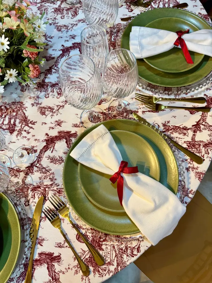 Detalhe de mesa posta com toalha toile vermelha, prato verde e guardanapo branco com fita vermelha